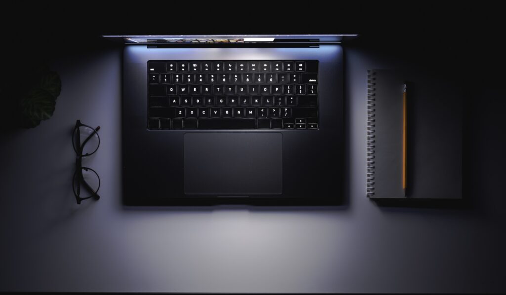 laptop with a glowing screen on a table in the dark, top view, copy space.